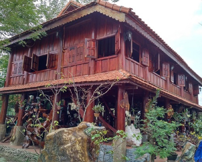 Nhà sàn gỗ truyền thống Việt Nam với mái ngói đỏ và cây xanh xung quanh.