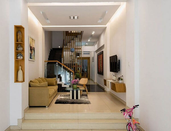 Phòng khách hiện đại với ghế sofa, cầu thang gỗ, và xe đạp trẻ em, mang lại cảm giác ấm cúng và tiện nghi.