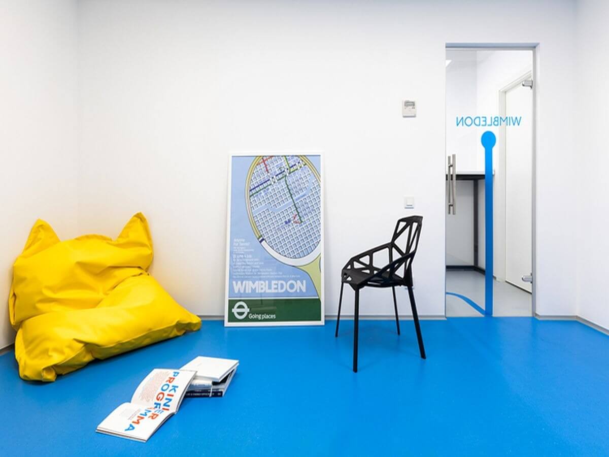 Căn phòng hiện đại với túi lười vàng, ghế đen và poster Wimbledon trên nền sàn màu xanh tươi sáng.