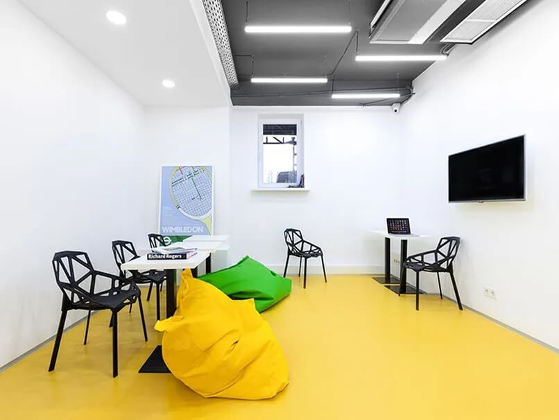 Phòng họp hiện đại với bàn ghế độc đáo, ghế lười màu vàng và xanh, bảng hiệu Wimbledon, tivi treo tường.