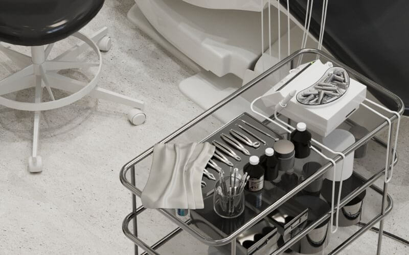 Dụng cụ y tế trên xe đẩy trong phòng khám nha khoa, bao gồm kéo, kéo cắt và chai thuốc.