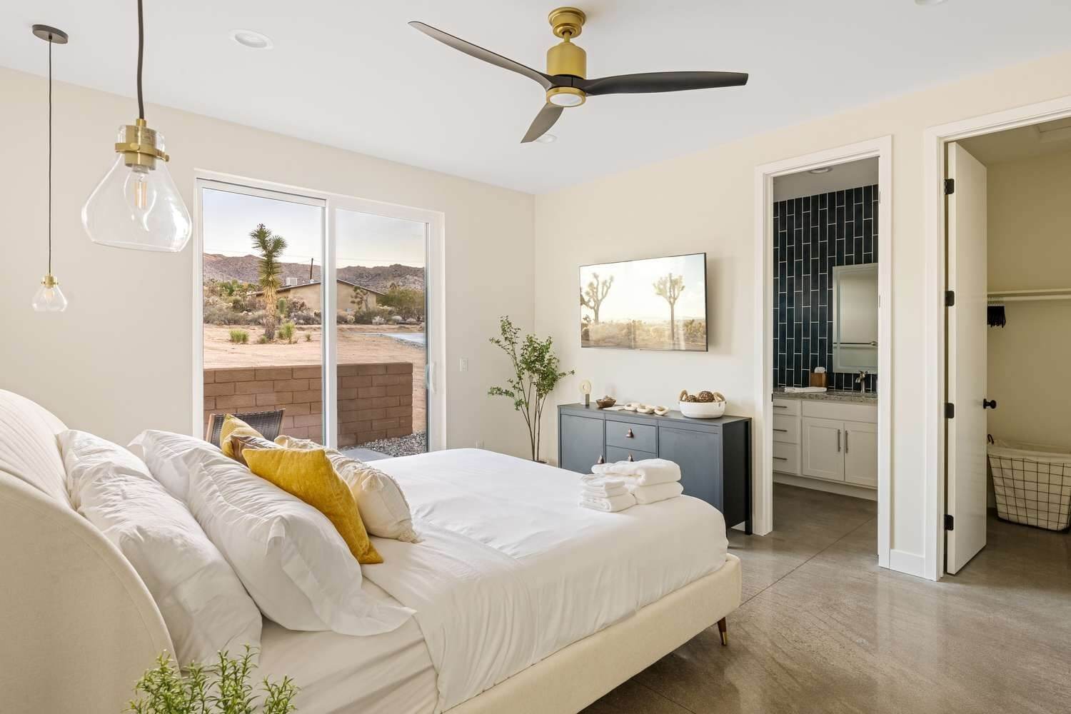 Phòng ngủ hiện đại, sáng sủa với giường lớn, quạt trần và cửa kính nhìn ra ngoài trời sa mạc.