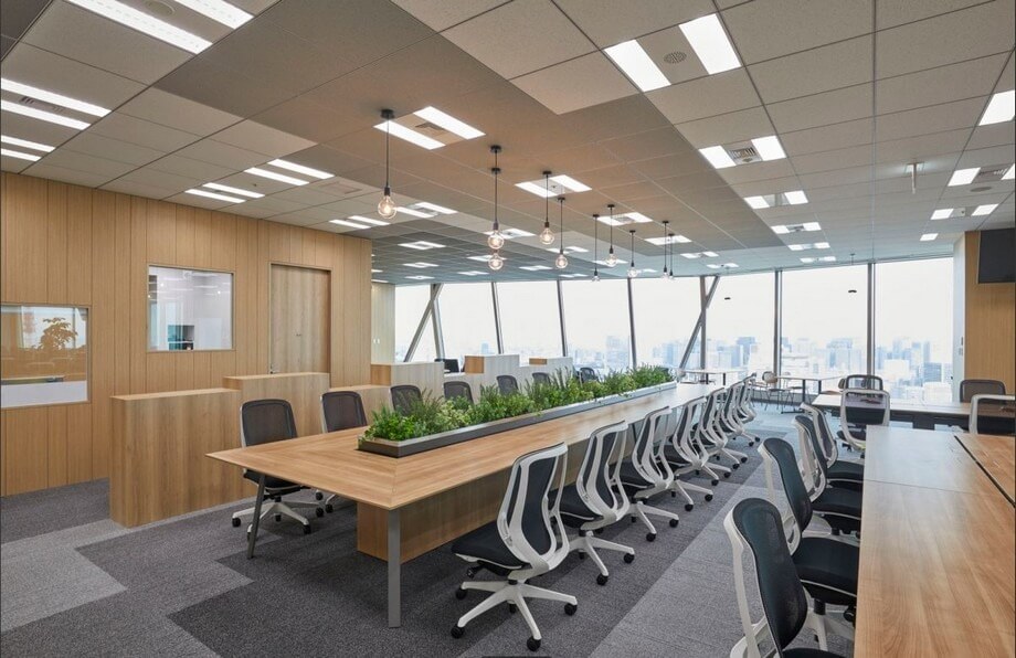 Văn phòng hiện đại với bàn dài, ghế xoay trắng và cây xanh trang trí, cửa sổ lớn nhìn ra quang cảnh thành phố.