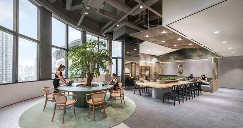 Văn phòng hiện đại với nội thất sang trọng, cây xanh lớn và bàn ghế thoải mái, tạo không gian làm việc thoải mái.