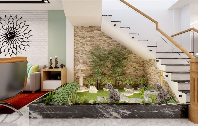 Góc vườn tiểu cảnh dưới cầu thang với cây xanh và đá trang trí, tạo không gian thư giãn trong nhà hiện đại.