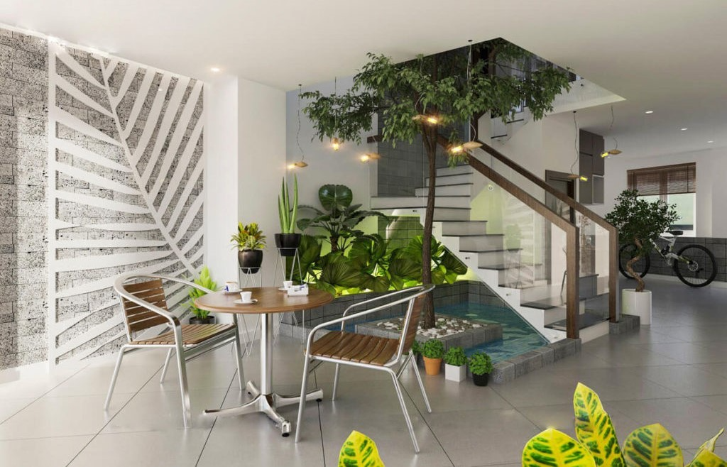 Phòng khách hiện đại với cây xanh, bàn tròn và cầu thang kính, tạo không gian thoải mái và gần gũi với thiên nhiên.