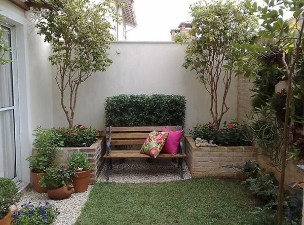 Ghế gỗ trong vườn nhỏ với cây xanh và hoa, tạo không gian thư giãn thoải mái.