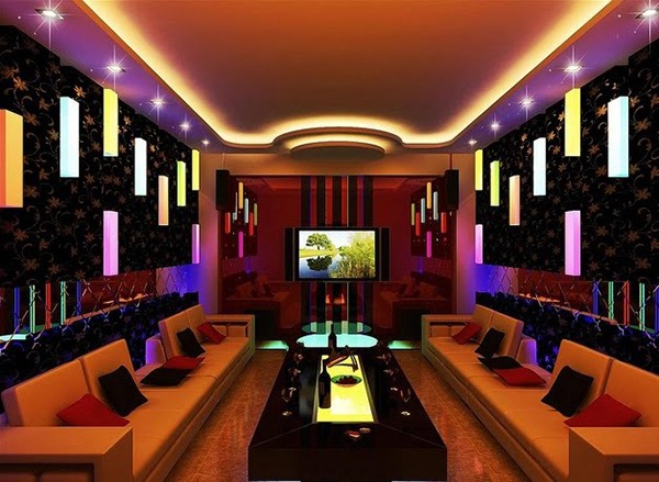 Phòng karaoke hiện đại với ánh sáng nhiều màu sắc, sofa thoải mái và màn hình TV lớn ở trung tâm.