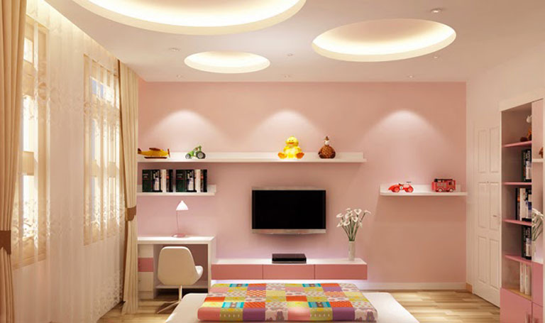 Phòng ngủ trẻ em màu hồng với giường sắc màu, TV treo tường, kệ sách và đèn trần hiện đại.