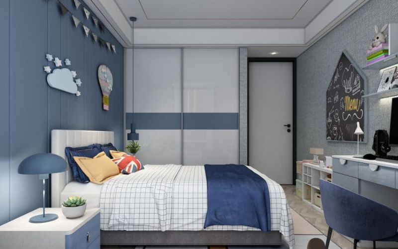 Phòng ngủ trẻ em màu xanh, giường có gối hoa văn, bảng đen trang trí, đèn bàn và bàn học bên cạnh.