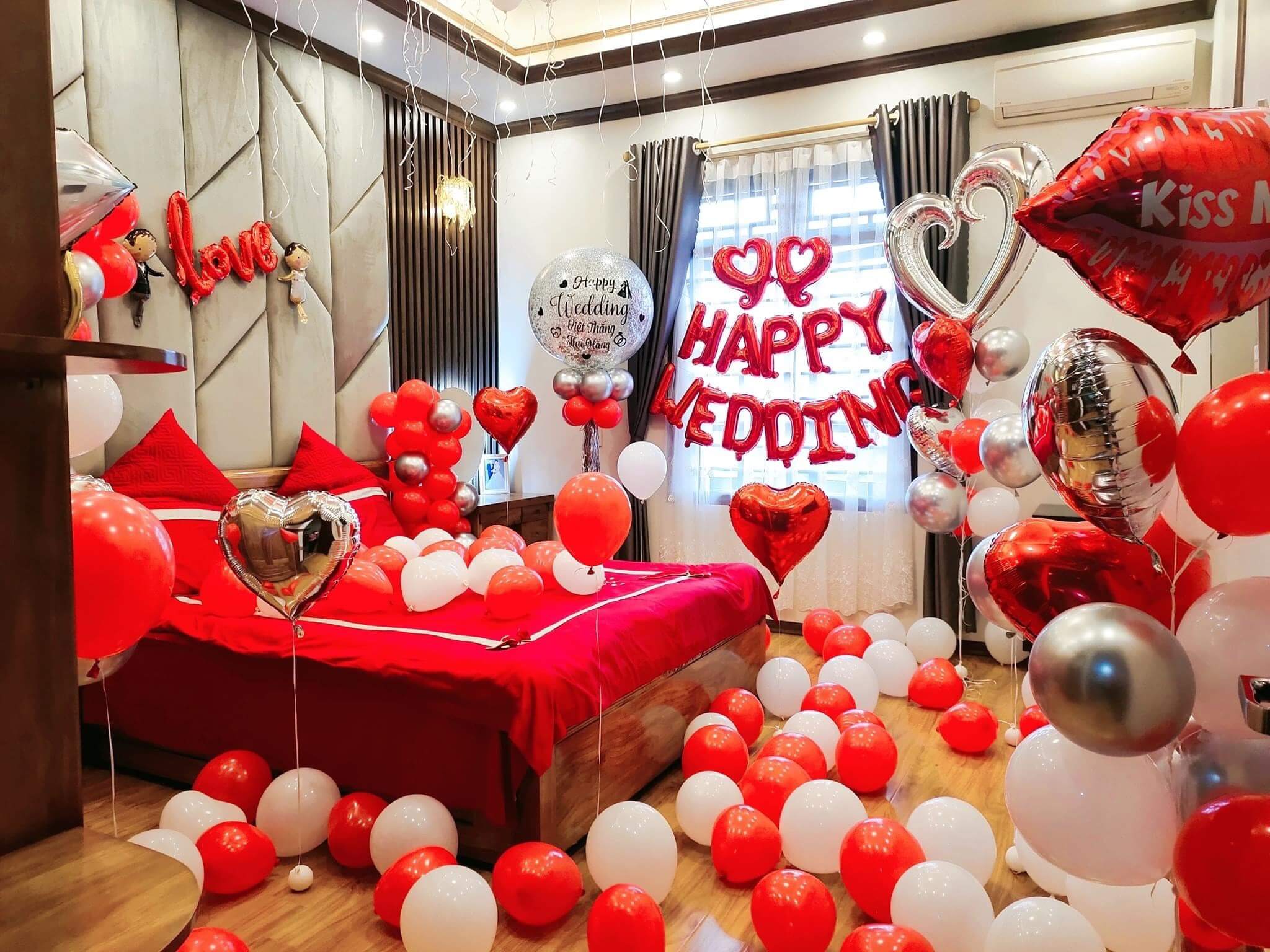 Phòng cưới trang trí bong bóng đỏ trắng, chữ Happy Wedding, giường đỏ, tạo không gian lãng mạn cho ngày đặc biệt.