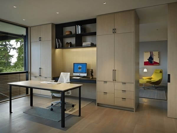 Văn phòng hiện đại với bàn làm việc, ghế xoay, máy tính, kệ sách, ánh sáng tự nhiên và phòng đọc thư giãn bên cạnh.