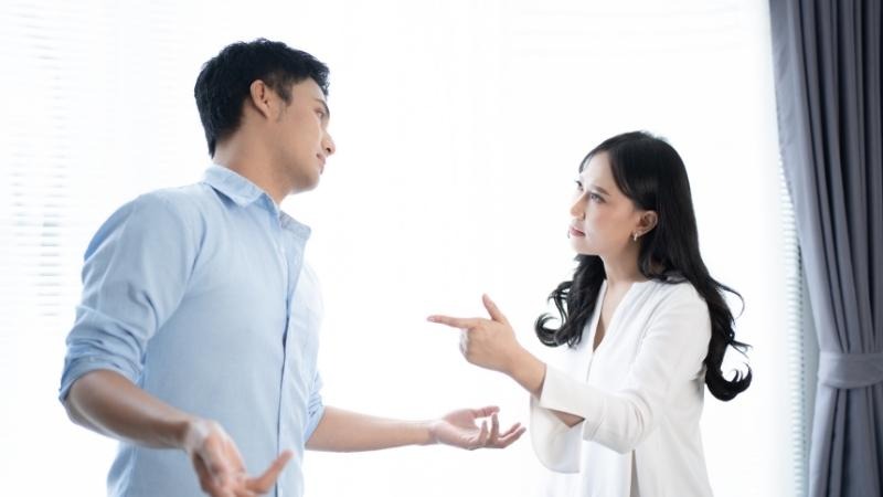 Cặp đôi trẻ tranh cãi trong phòng khách; người phụ nữ chỉ tay, người đàn ông giơ tay lên trong sự bất đồng.