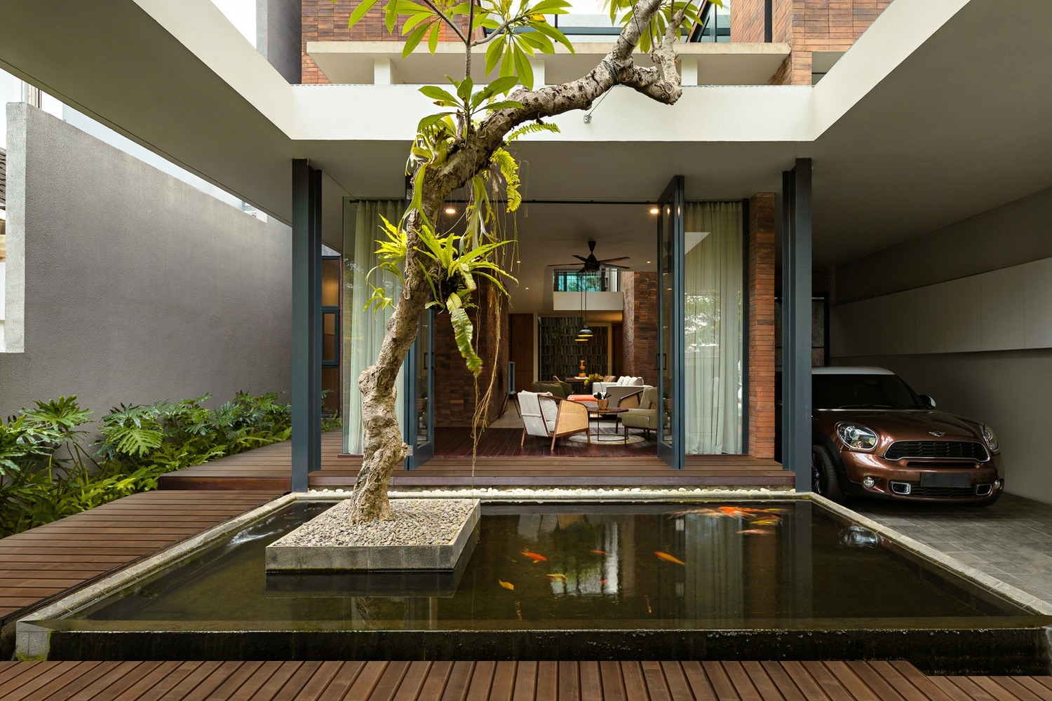 Nhà hiện đại với hồ cá ở sân trước, cây cảnh và gara ô tô bên cạnh.