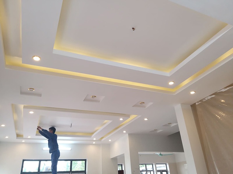 Công nhân lắp đặt đèn trên trần nhà thạch cao với thiết kế hiện đại và hệ thống chiếu sáng tích hợp.
