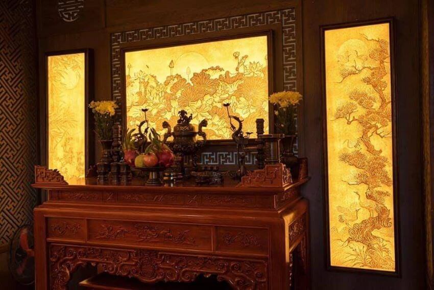 Bàn thờ gỗ truyền thống với đèn nền vàng ấm áp và bố trí hoa, trái cây trang nhã tại không gian thờ cúng.