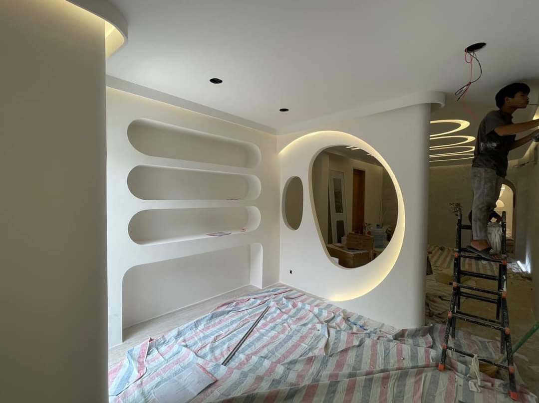 tuong-thach-cao Không gian nội thất hiện đại với giá đỡ và gương tròn, công nhân đang làm việc trên thang.