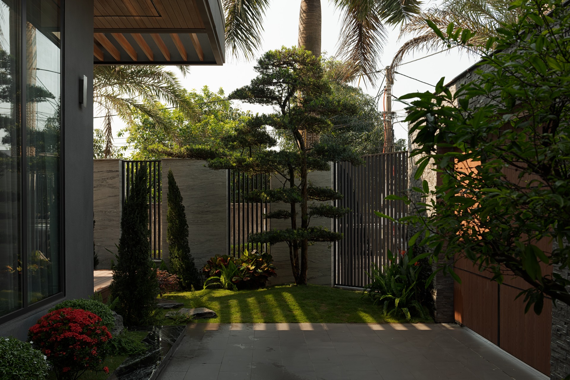 umi6896-enhanced-nr-edit Khu vườn xanh mát với cây cối và hoa tươi bên cạnh ngôi nhà hiện đại, ánh nắng len qua hàng cây.