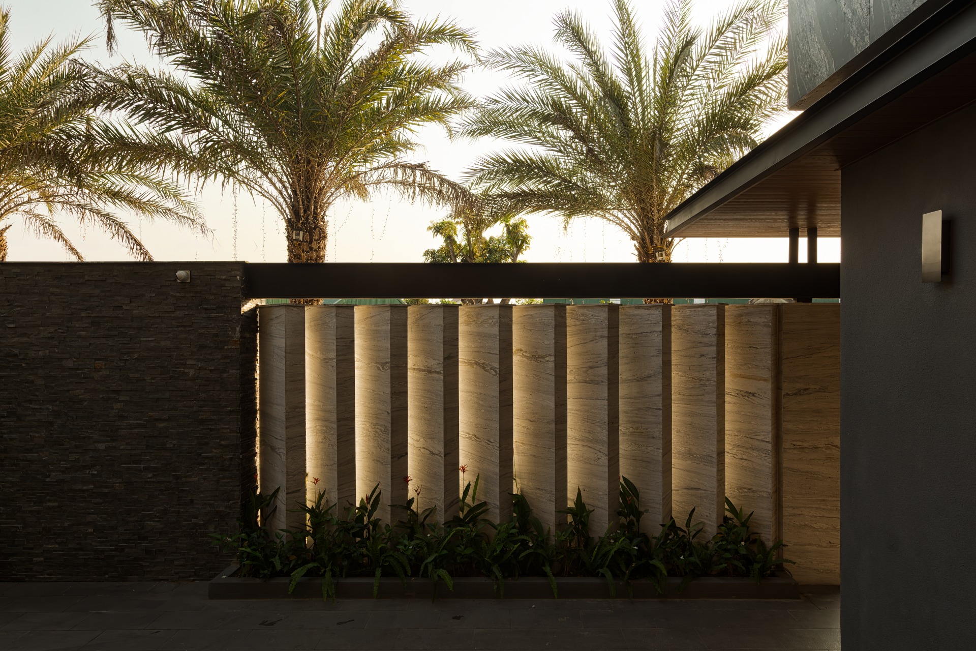 umi8726-enhanced-nr-edit Hàng cây cọ sau tường đá hiện đại được chiếu sáng nhẹ nhàng trong ánh hoàng hôn.