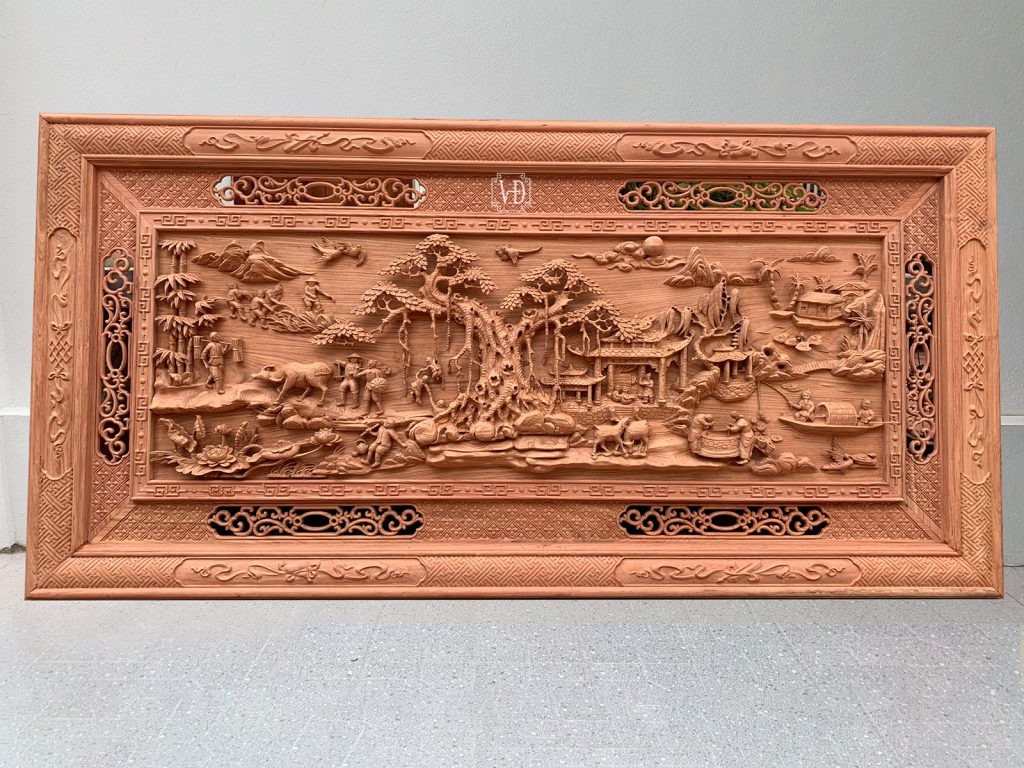 Tranh gỗ chạm khắc cảnh đồng quê, bao gồm nhà tranh, cây cối, người và động vật, mang đậm nét văn hóa truyền thống.