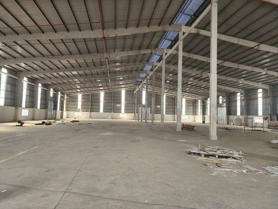 Kho hàng trống rộng lớn với trần cao và kết cấu kim loại, ánh sáng tự nhiên chiếu qua cửa sổ.
