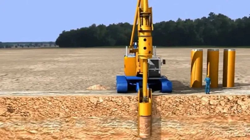 Máy khoan đang hoạt động trên công trường xây dựng với ống khoan lớn và công nhân tại hiện trường.