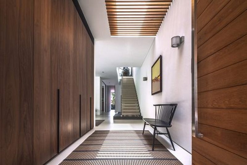 Lối vào hiện đại với sàn gỗ, thảm sọc và ghế ngồi, cầu thang nổi bật phía xa.