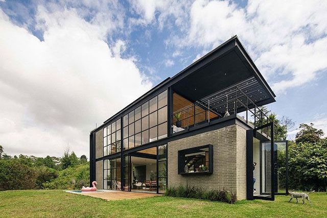 Nhà kính hiện đại trên thảm cỏ xanh, kiến trúc độc đáo với cửa kính lớn, thiết kế mở thoáng đãng và gần gũi thiên nhiên.