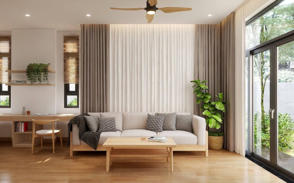 Phòng khách hiện đại với sofa màu be, cây xanh và cửa sổ lớn, tạo không gian thoáng mát và sáng sủa.