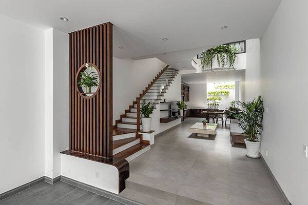 Nhà hiện đại với cầu thang trắng, tường gỗ và cây xanh trang trí, không gian mở thoáng đãng.