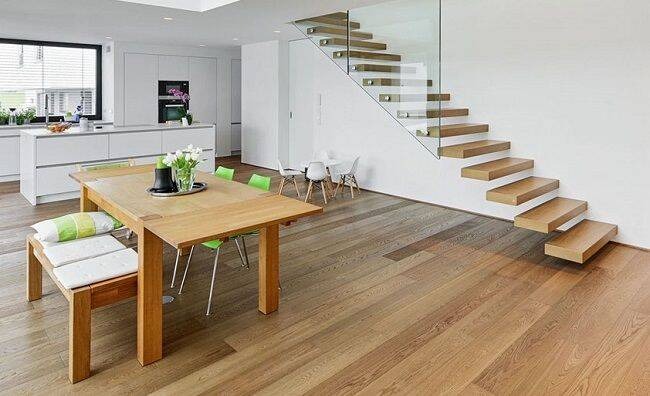Nhà bếp hiện đại với bàn gỗ, cầu thang nổi, nội thất tối giản và sàn gỗ sáng màu.