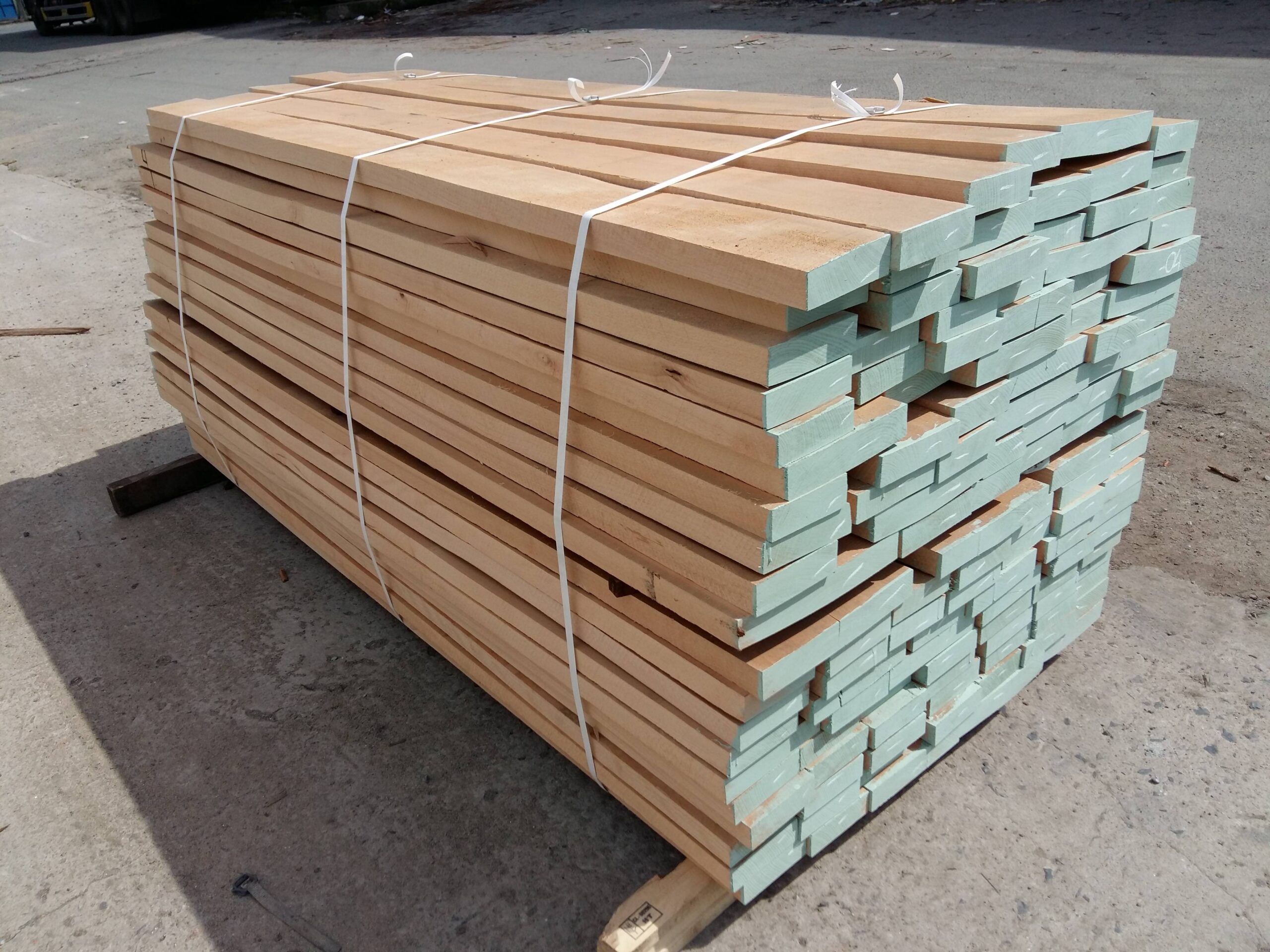 Đống gỗ xẻ vuông vắn xếp chồng trên pallet, được buộc dây nhựa chắc chắn chuẩn bị vận chuyển.