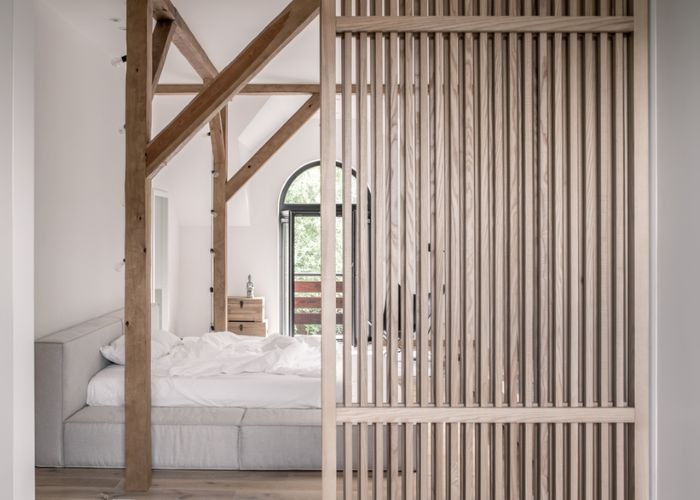 Phòng ngủ tối giản với cửa sổ vòm và khung gỗ, giường xám nhạt, tạo không gian ấm cúng và thanh lịch.