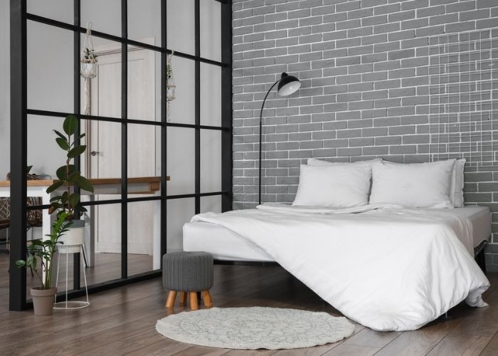 Phòng ngủ hiện đại với giường trắng, gạch xám, đèn sàn và cây xanh, mang lại cảm giác thoải mái và tinh tế.