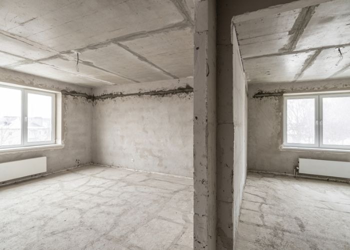 Căn phòng bê tông chưa hoàn thiện với cửa sổ lớn, ánh sáng tự nhiên, không gian mở, tiềm năng thiết kế linh hoạt.