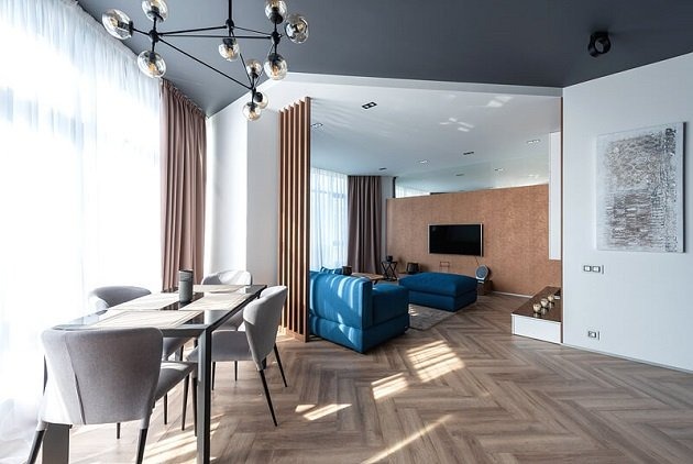 Phòng khách hiện đại với sofa xanh, bàn ăn và sàn gỗ, ánh sáng tự nhiên qua cửa sổ lớn, trang trí tối giản.