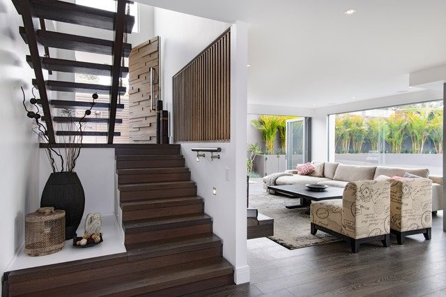 Nội thất phòng khách hiện đại với cầu thang gỗ sang trọng, sofa trung tính và cửa sổ lớn nhìn ra sân vườn.