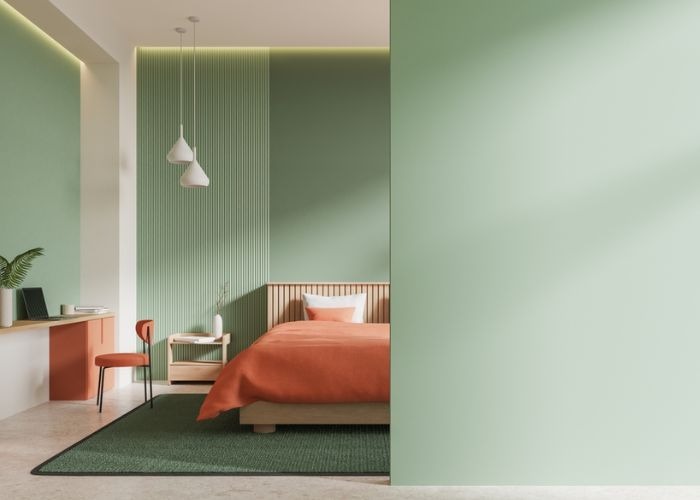 Phòng ngủ hiện đại với tông màu xanh và cam, có giường, bàn làm việc và ghế, tạo không gian tiện nghi và thoải mái.