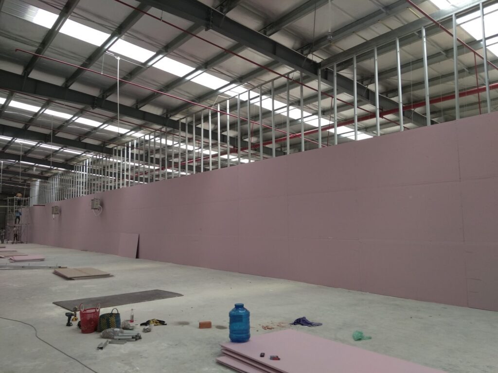 Nhà kho đang xây dựng với tường thạch cao màu hồng và khung kim loại. Công trường rộng và sáng sủa.
