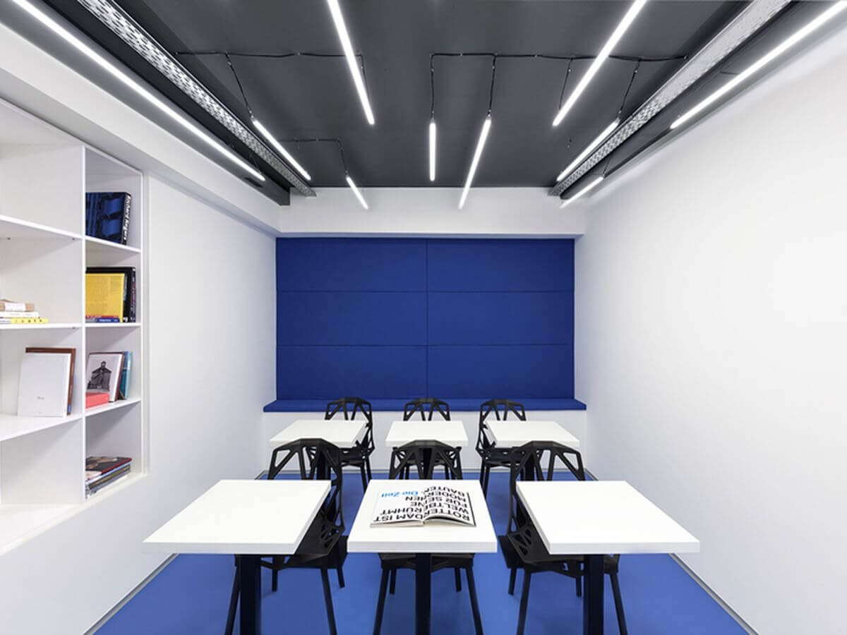 Phòng học hiện đại với bàn ghế trắng đen và kệ sách gọn gàng, ánh sáng đèn LED trên trần.