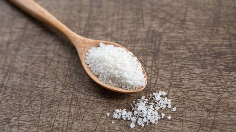 Muỗng gỗ đựng muối biển trên bàn gỗ nâu, thể hiện thành phần tự nhiên trong nấu ăn.