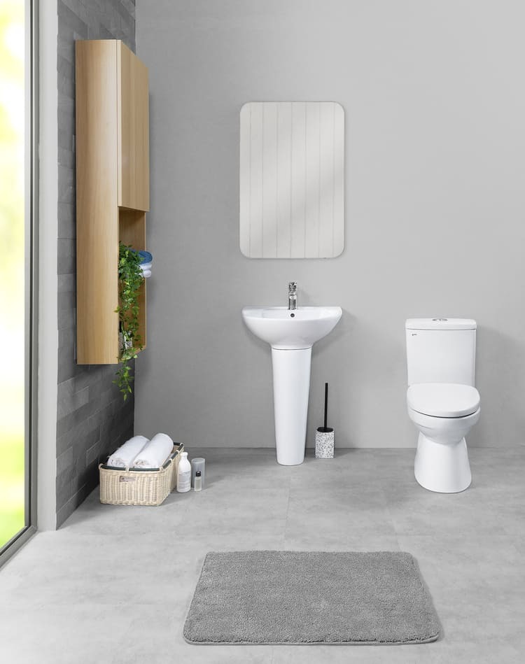 Phòng tắm hiện đại với bồn cầu, bồn rửa, tủ gỗ treo tường, thảm xám, và ánh sáng tự nhiên từ cửa sổ.