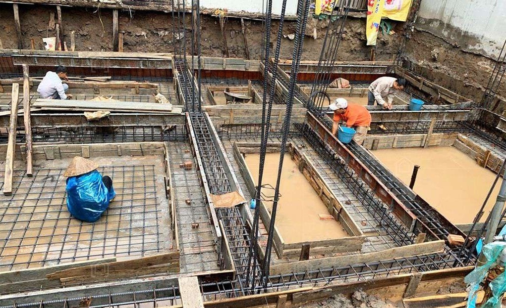 Công nhân xây dựng thi công móng nhà, cốt thép và gỗ bao quanh khu vực nền ngập nước.