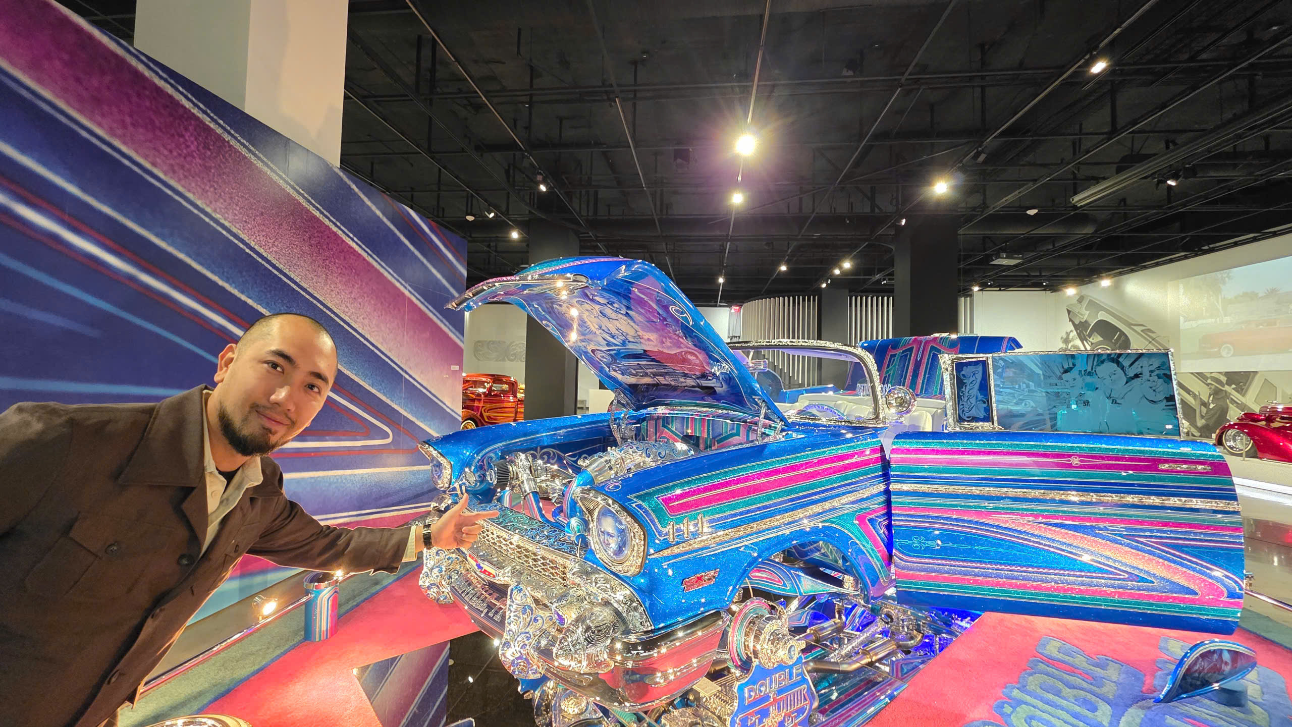 z6689752493271_738cebda05507b21a15a52bdf449d0df Người đàn ông đứng cạnh ô tô cổ màu xanh lấp lánh tại triển lãm xe hơi trong nhà.