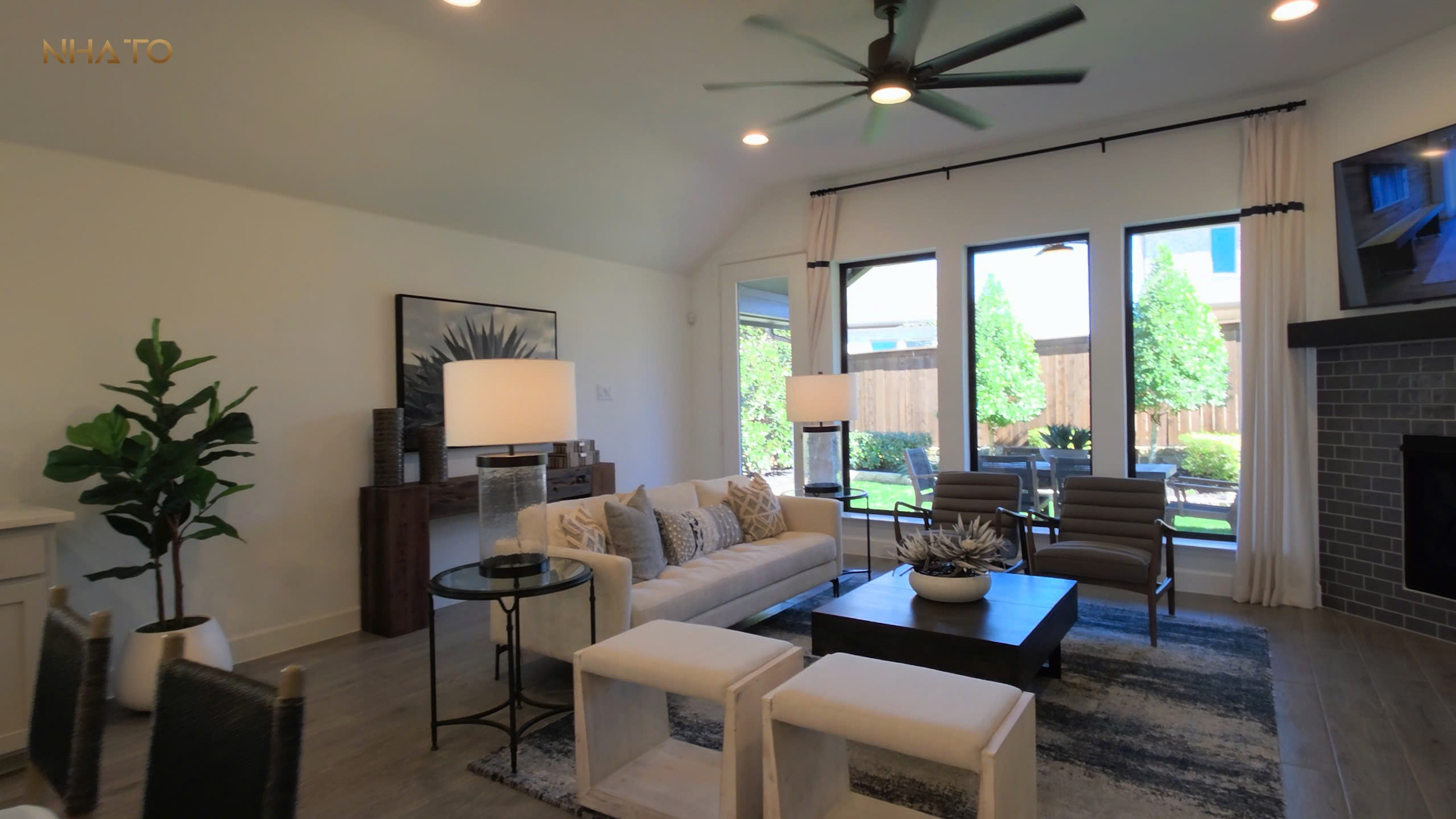 Phòng khách hiện đại với sofa trắng, cây xanh, và cửa sổ lớn nhìn ra vườn.