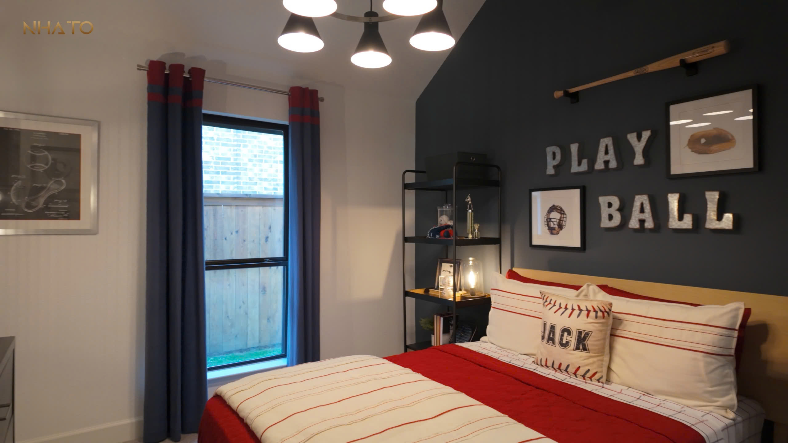 z6803397537015_f32ad6b2ca95c784fdb87f415d9e385f-1 Phòng ngủ thể thao với giường đỏ, gối bóng chày, đèn trần và trang trí chữ PLAY BALL trên tường.