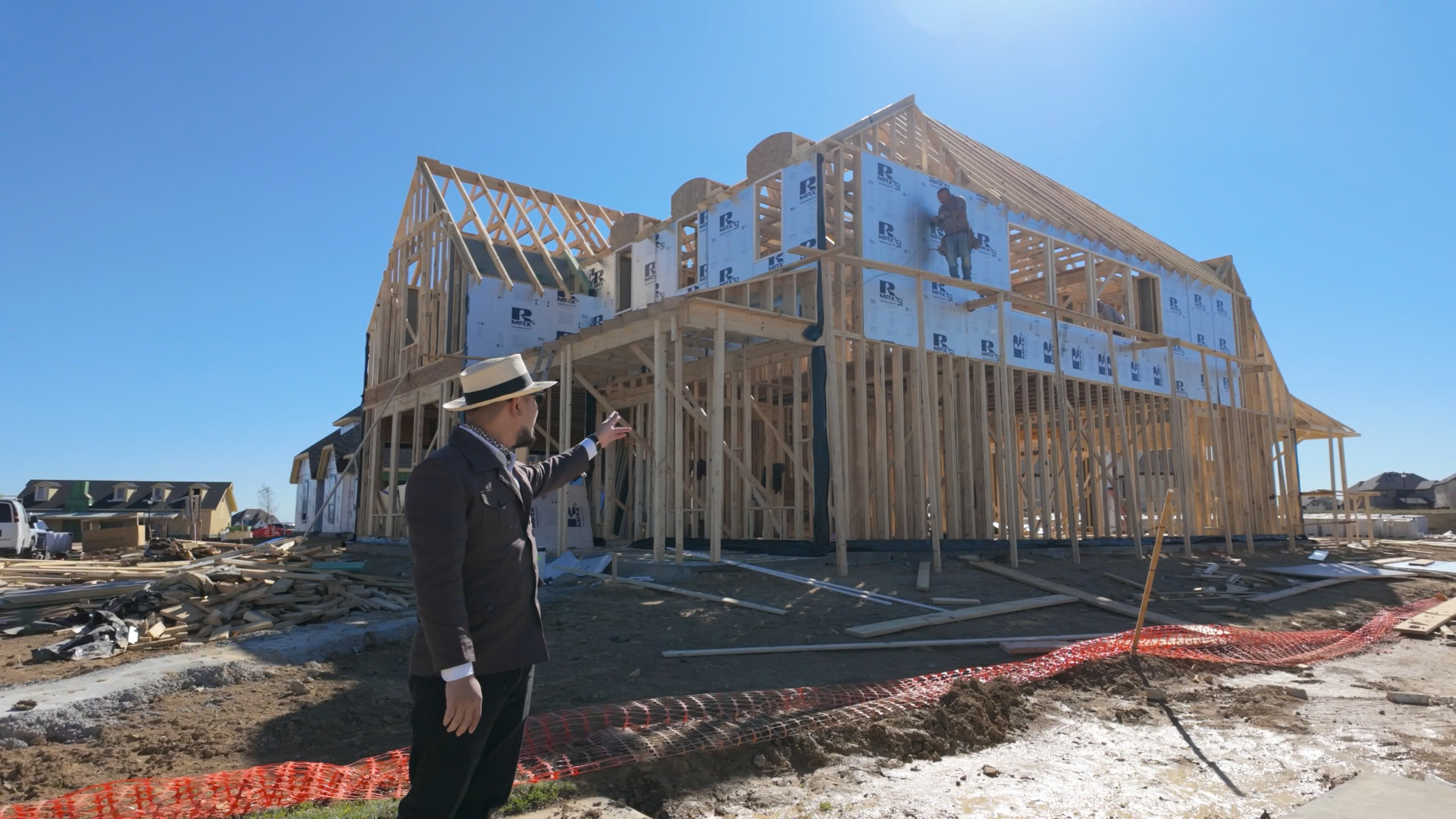 Người đàn ông đứng trước công trình xây dựng nhà gỗ dưới bầu trời xanh, ban ngày.