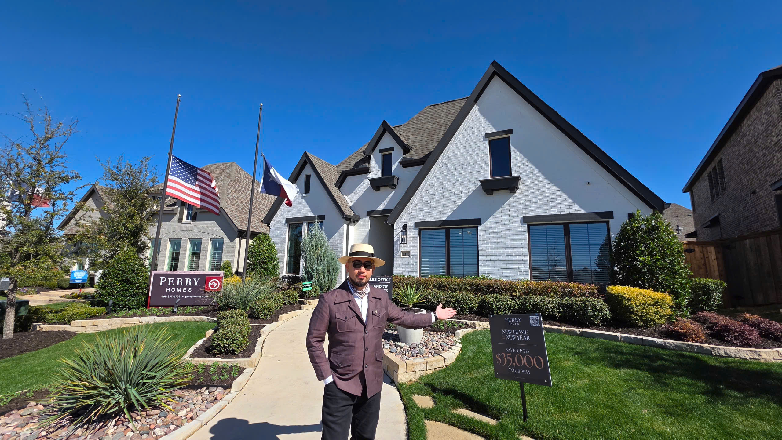 Người đàn ông trước ngôi nhà hiện đại, có bảng hiệu Perry Homes và cờ Mỹ. Trời trong xanh, nắng đẹp.
