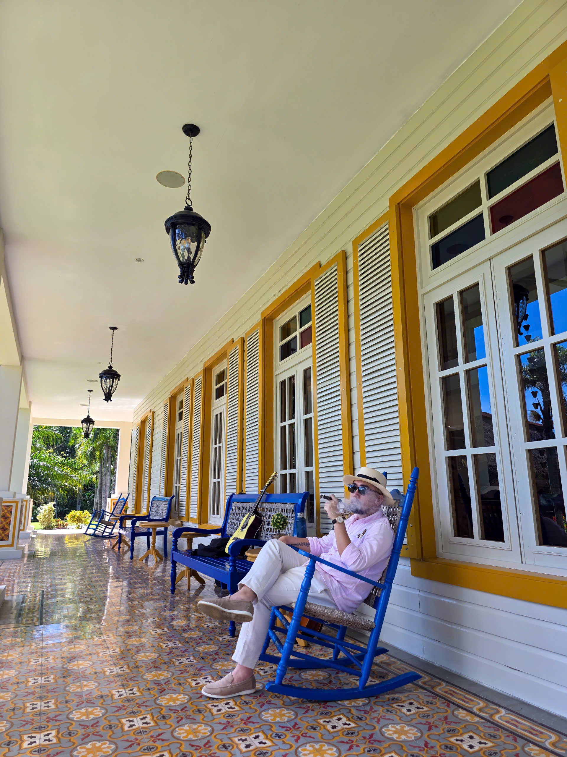 z6865888903550_e381c288def43909d192e635a744c805 Người đàn ông thư giãn trên ghế bập bênh, thưởng thức cà phê tại ban công ngôi nhà phong cách cổ điển.