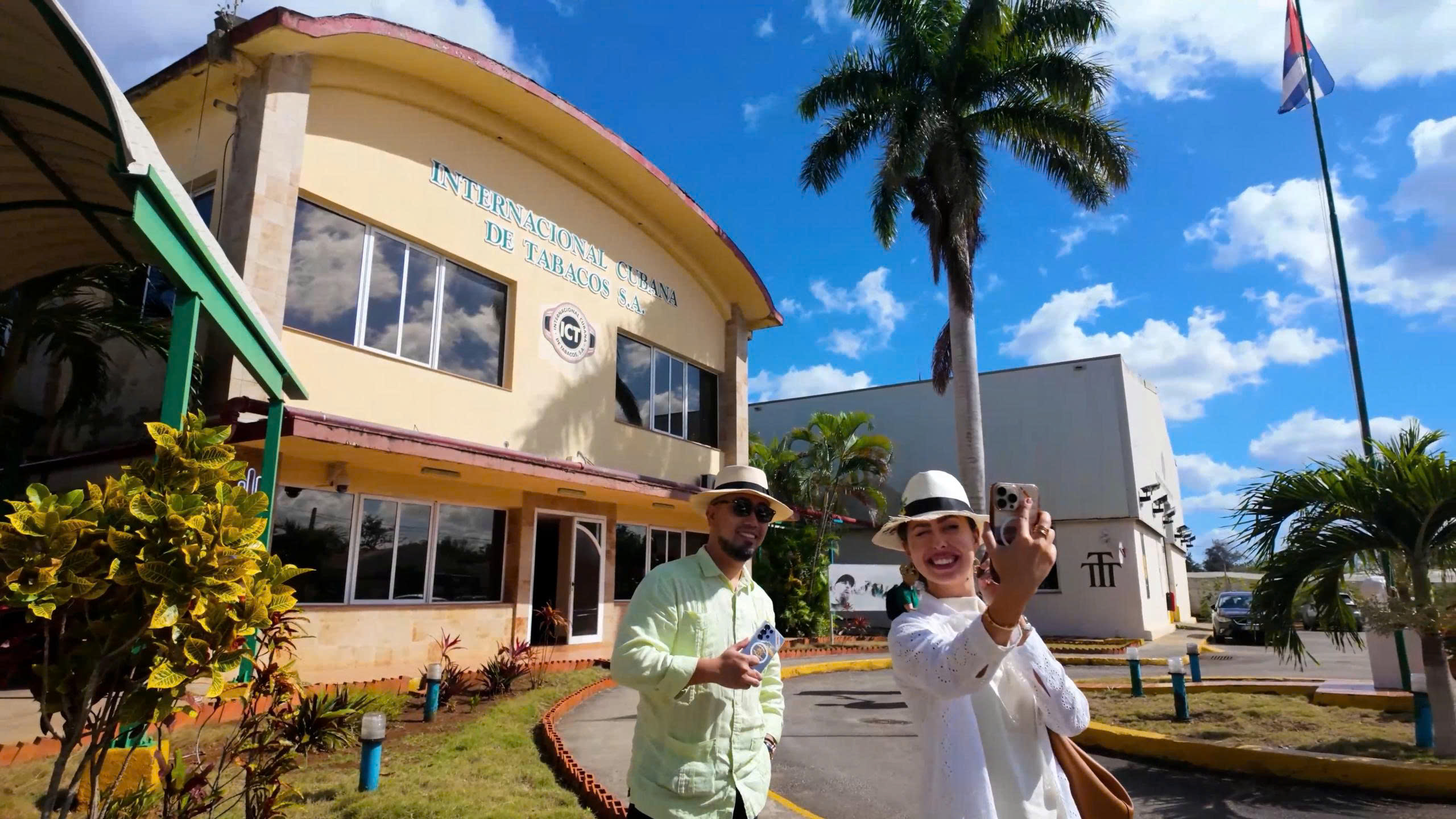 z6879709757814_f583e4110e9a10fedeafdfeeee9d2c20-1 Người đàn ông và phụ nữ chụp selfie trước tòa nhà Internacional Cubana de Tabacos S.A., trời trong xanh.